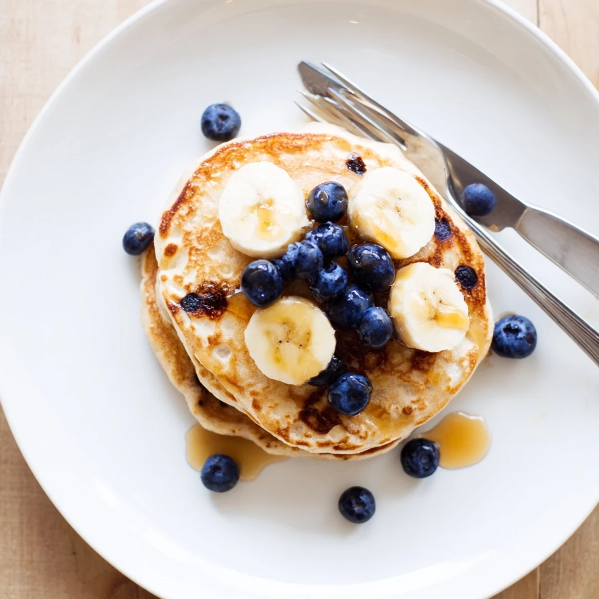 Stack of fluffy protein banana pancakes topped with fresh maple syrup and sliced bananas