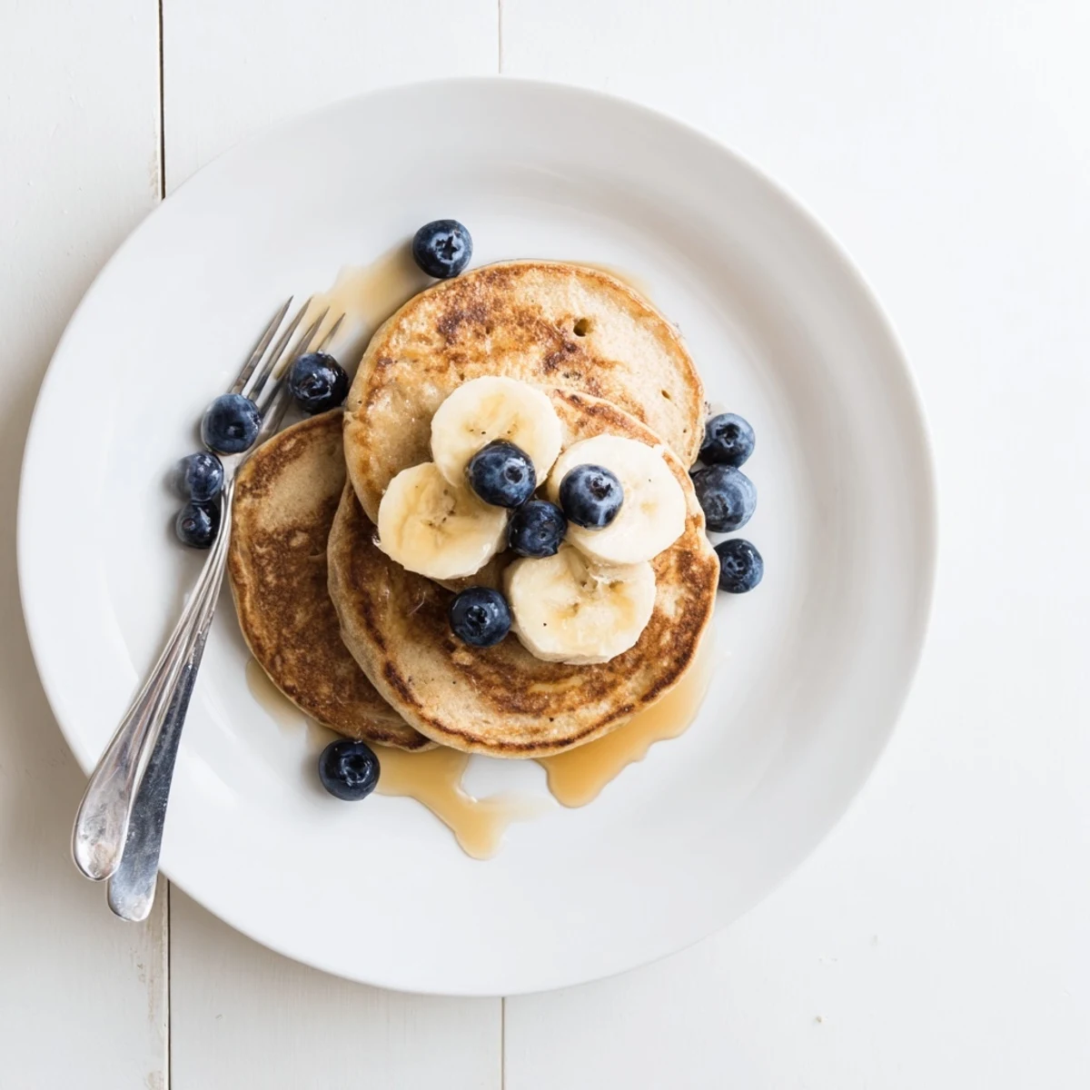 Golden brown protein banana pancakes cooking in a skillet with visible bubble texture