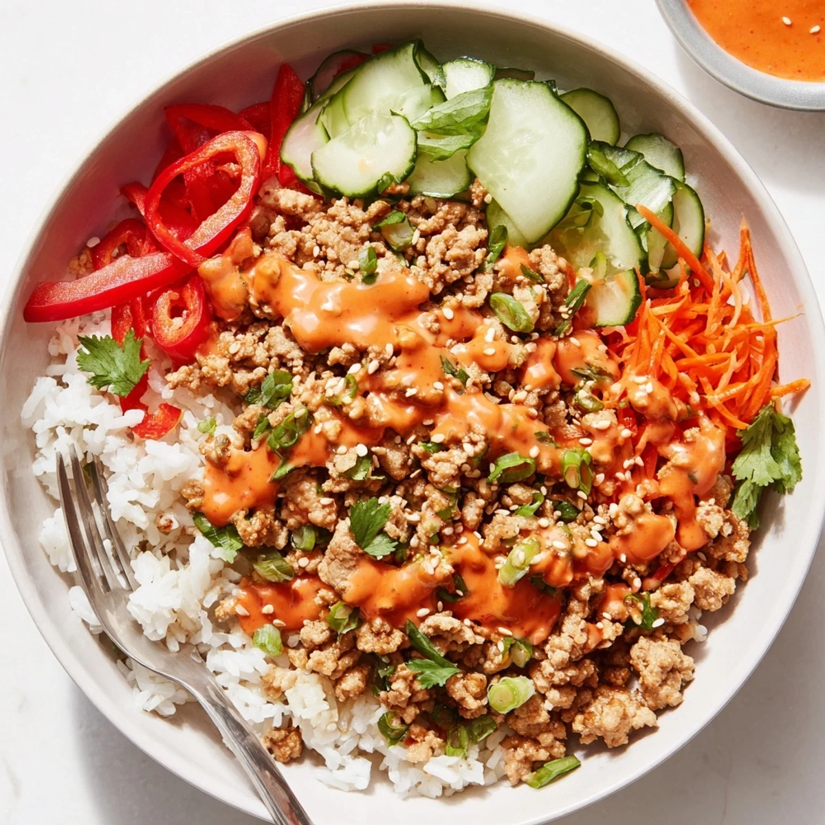Ground turkey rice bowls with bang bang sauce topped with shredded carrots and sesame seeds