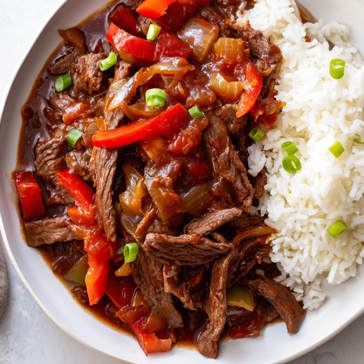 Slow Cooker Pepper Steak served steaming hot over fluffy white rice with green onion garnish