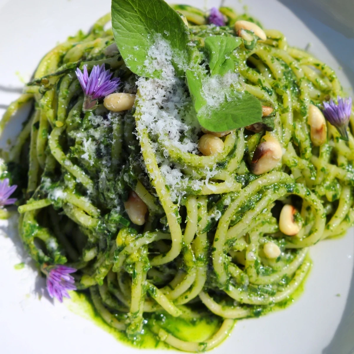 Steaming plate of wild garlic pesto pasta garnished with fresh edible spring flowers