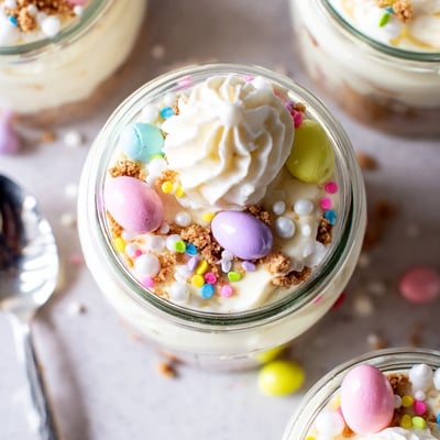 Individual Easter Egg Cheesecake Jars topped with whipped cream and festive pastel sprinkles for spring parties