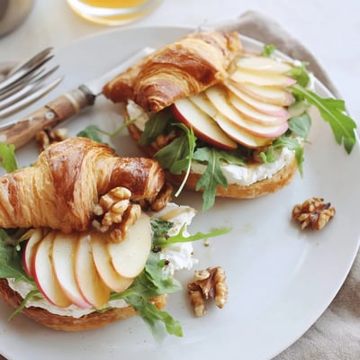 Open-faced Apple Goat Cheese Croissant Sandwich layered with arugula, honey, and walnuts.