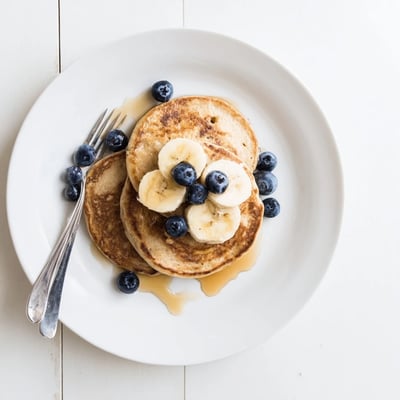 Golden brown protein banana pancakes cooking in a skillet with visible bubble texture